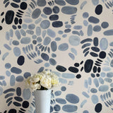 A vase of flowers stands in front of a wall covered in a playful paint blotch print in blue and gray on a cream field.