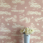 A vase of flowers stands in front of a wall covered in a playful illustrated car crash print in cream, white and mauve.