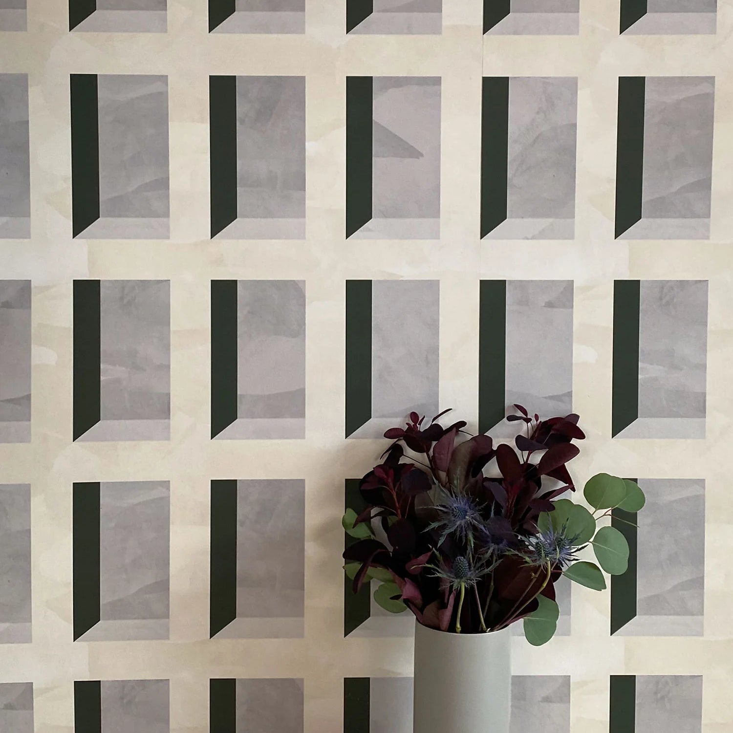 A vase of flowers stands in front of a wall papered in a dimensional grid print in shades of cream, gray and charcoal.