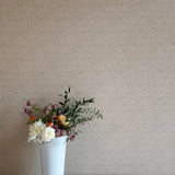 A vase of flowers stands in front of a wall papered in a painterly leaf print in black on a greige field.