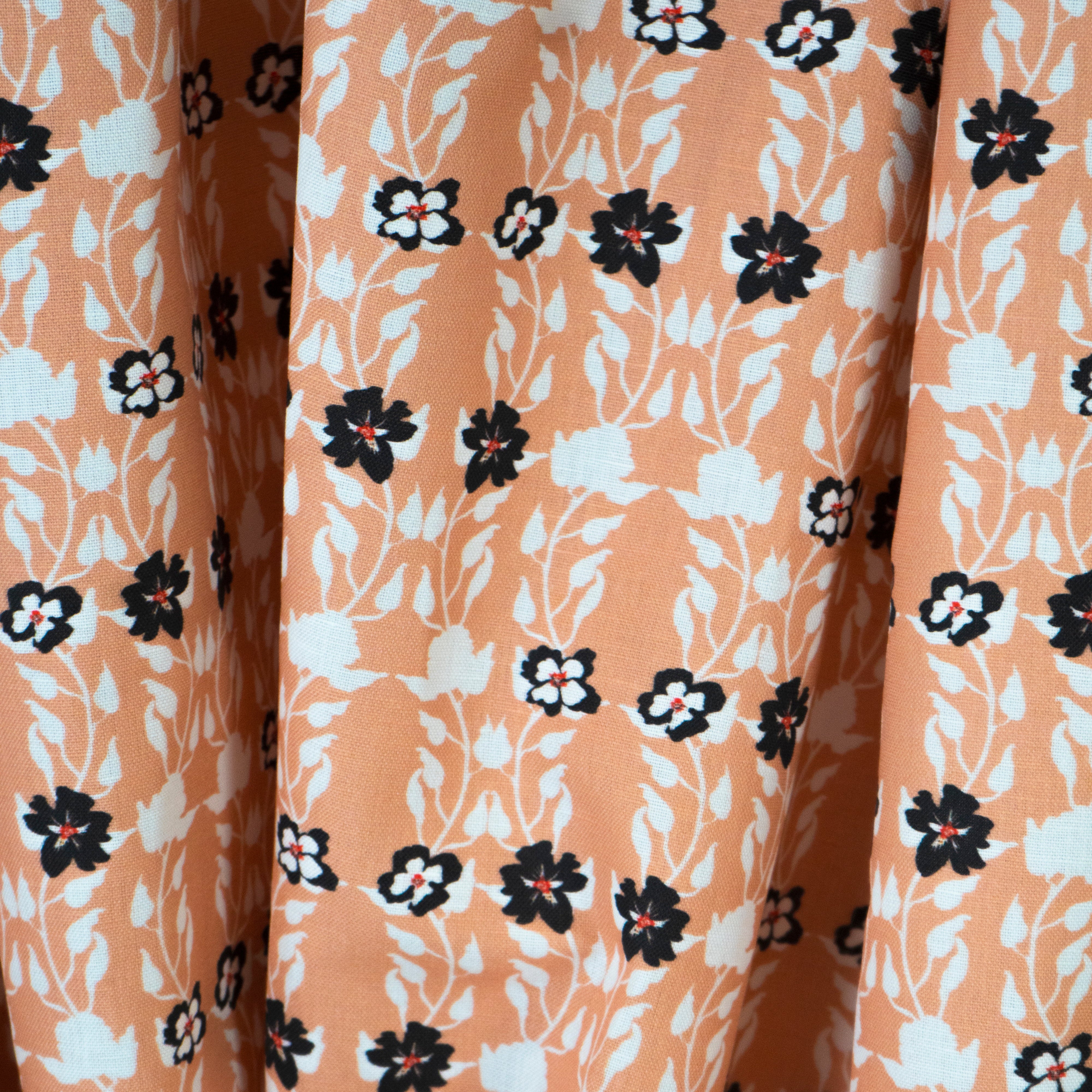 Draped fabric yardage in a linear floral print in red, white and black on an orange field.