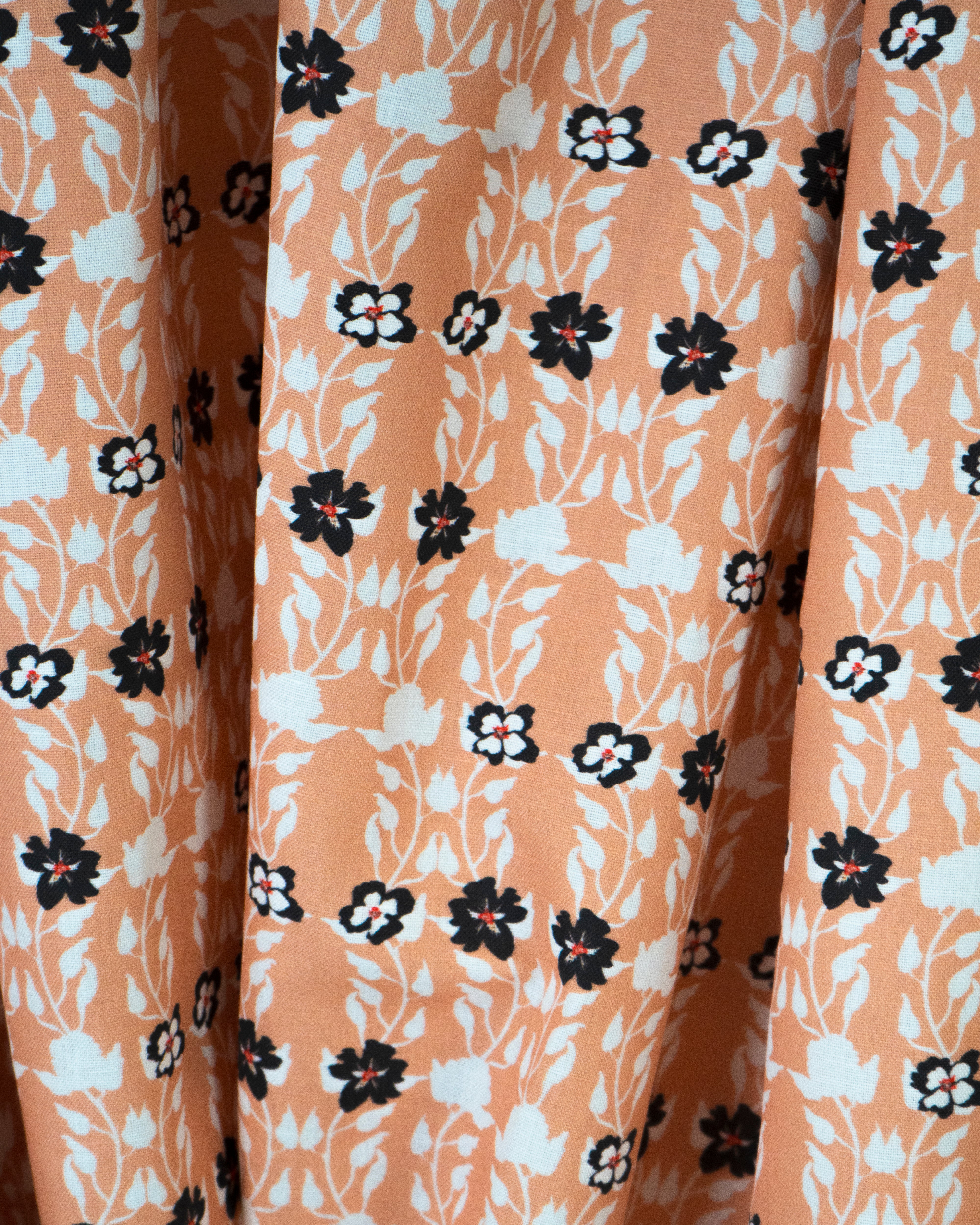 Draped fabric yardage in a linear floral print in red, white and black on an orange field.