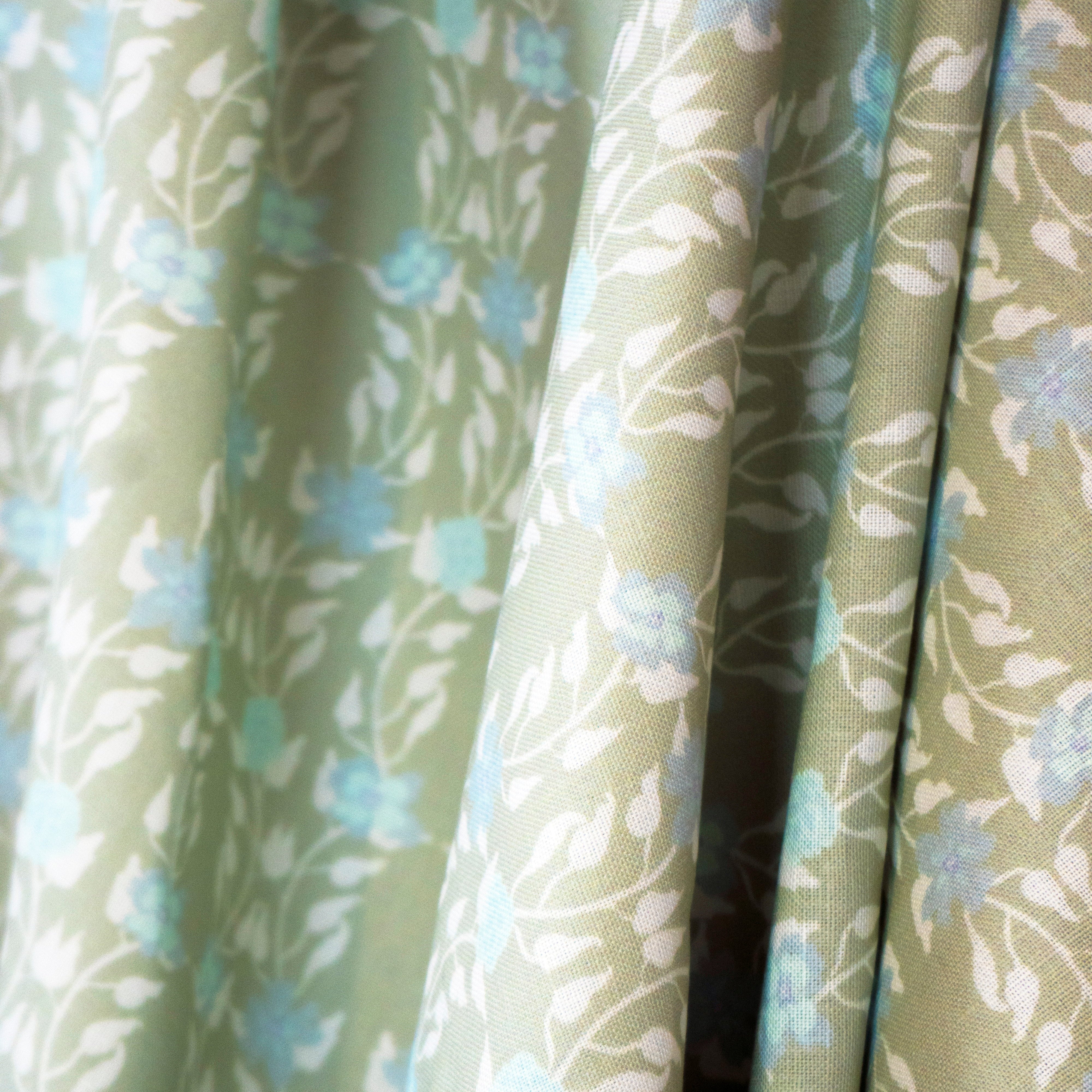 Draped fabric yardage in a linear floral print in blue and white on a green field.