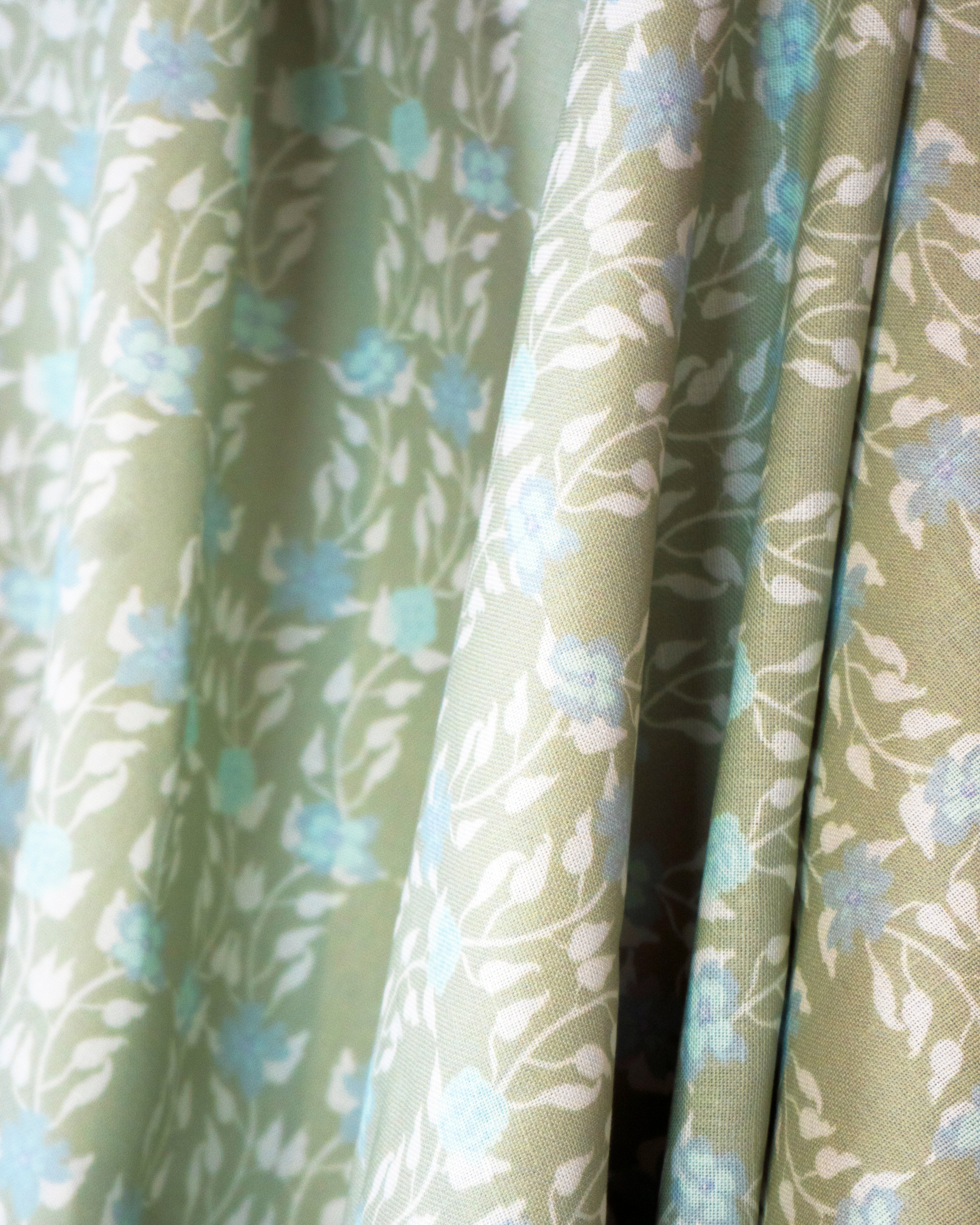 Draped fabric yardage in a linear floral print in blue and white on a green field.