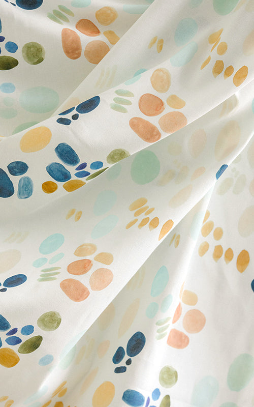 Draped fabric yardage in an abstract painterly print in shades of turquoise, blue and orange on a white field.