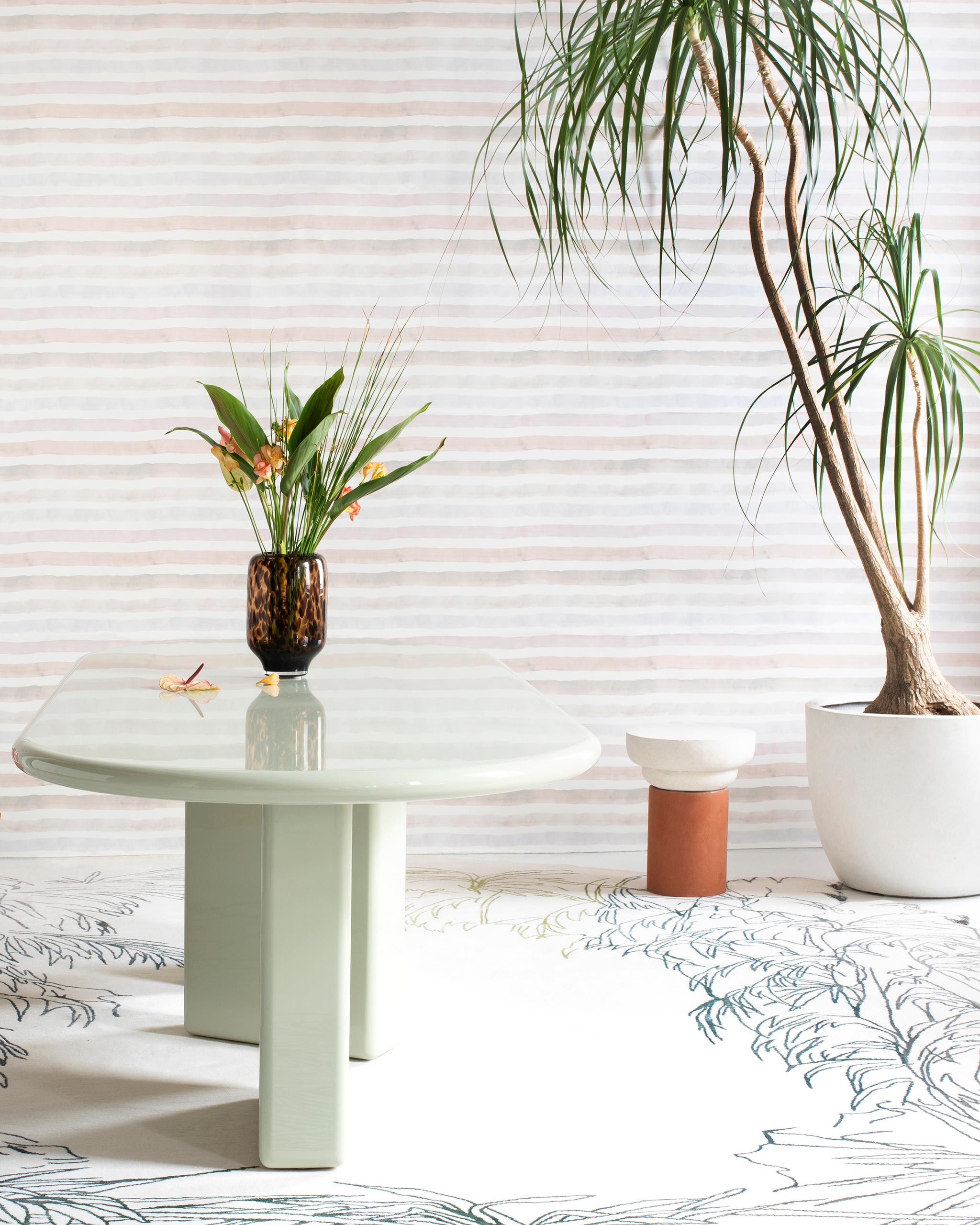 A modernist living space filled with plants and an accent wall papered in a painterly stripe print in pink, cream and white.