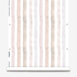 Partially unrolled wallpaper yardage in a painterly stripe print in shades of pink, gray and cream on a white field.