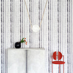 A modernist living tableau with a wall papered in a painterly stripe print in shades of gray on a white field.