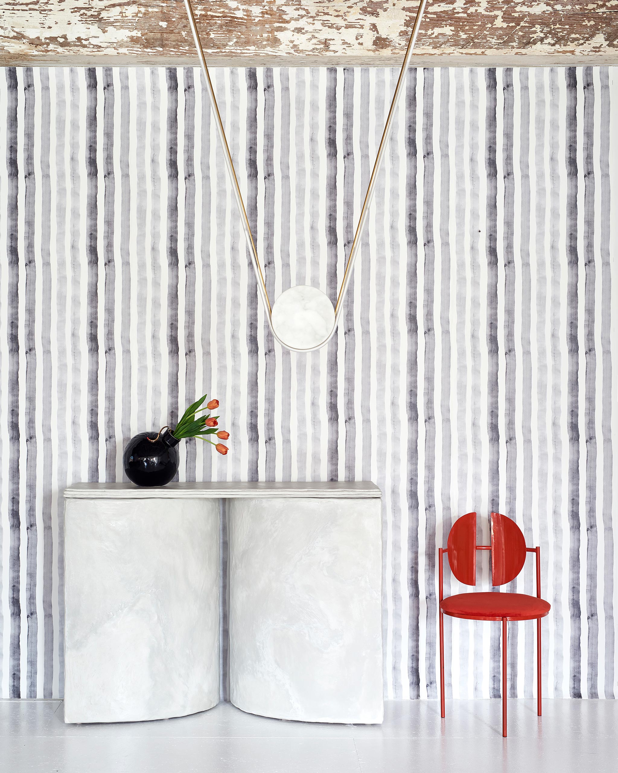 A modernist living tableau with a wall papered in a painterly stripe print in shades of gray on a white field.