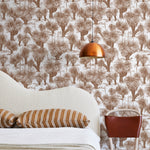 A modernist bed, hanging lamp and chair stand in front of a wall papered in a painterly tree print in rust and white.