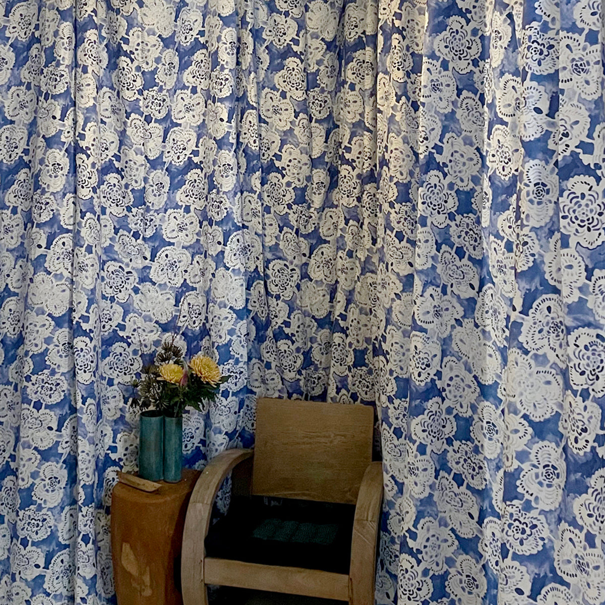 Blue and white floral patterned curtains with a wooden chair and small table in front.
