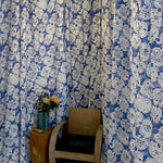 Blue and white floral patterned curtains with a wooden chair and small table in front.