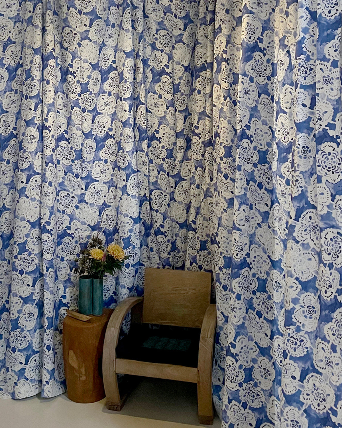 Blue and white floral patterned curtains with a wooden chair and small table in front.