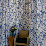 Blue and white floral patterned curtains with a wooden chair and small table in front.
