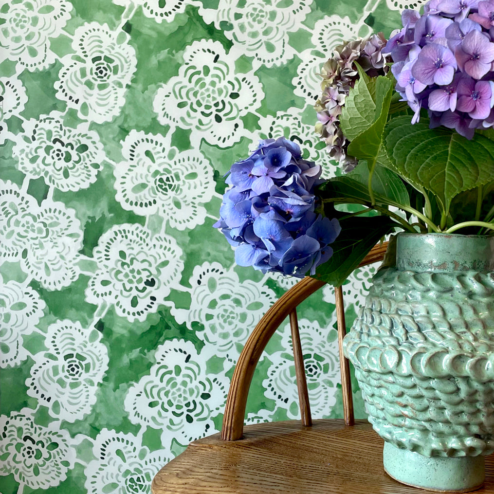 Decorative wallpaper with lace pattern, wooden stool, and floral arrangement.