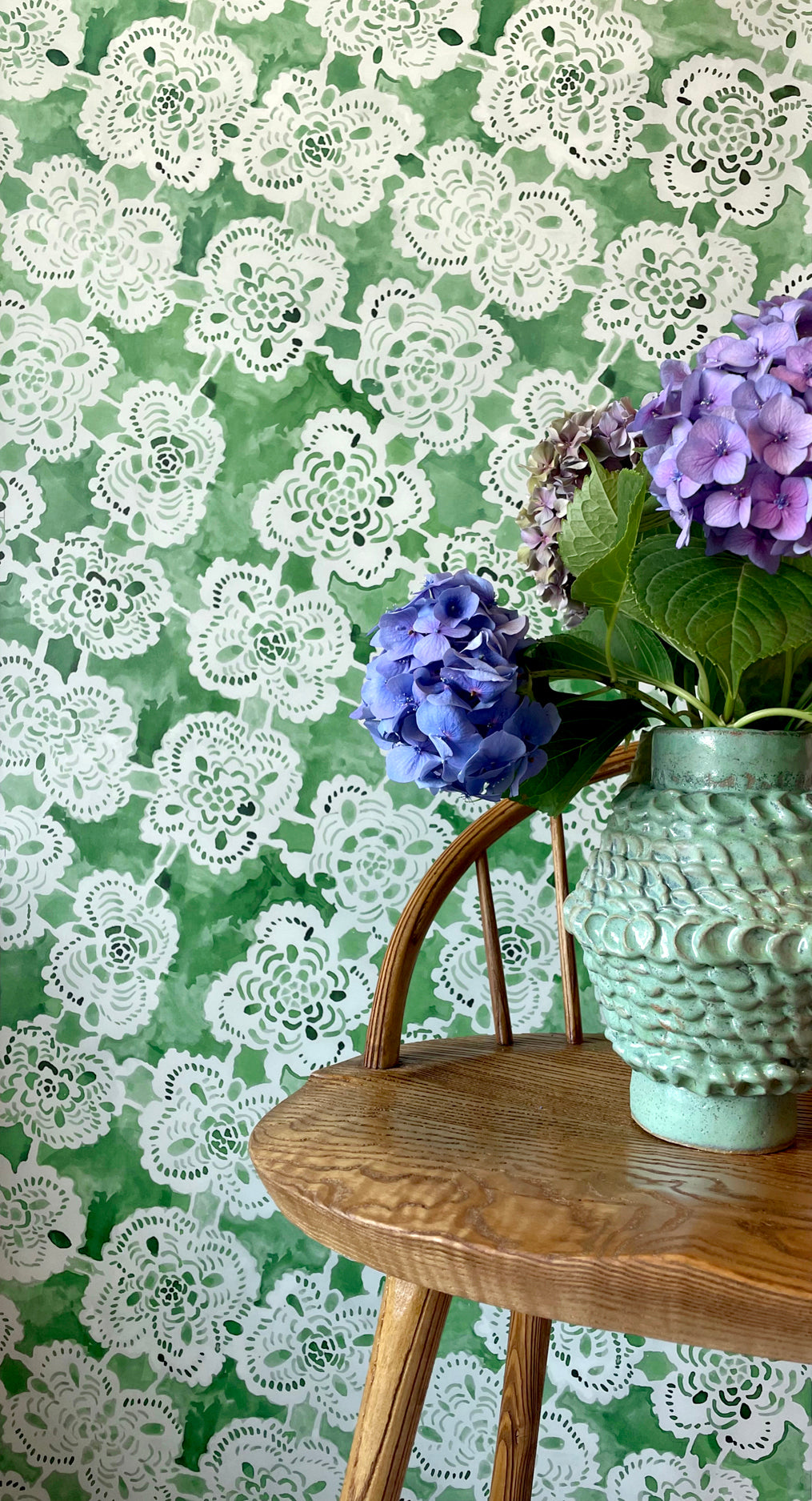 Decorative wallpaper with lace pattern, wooden stool, and floral arrangement.