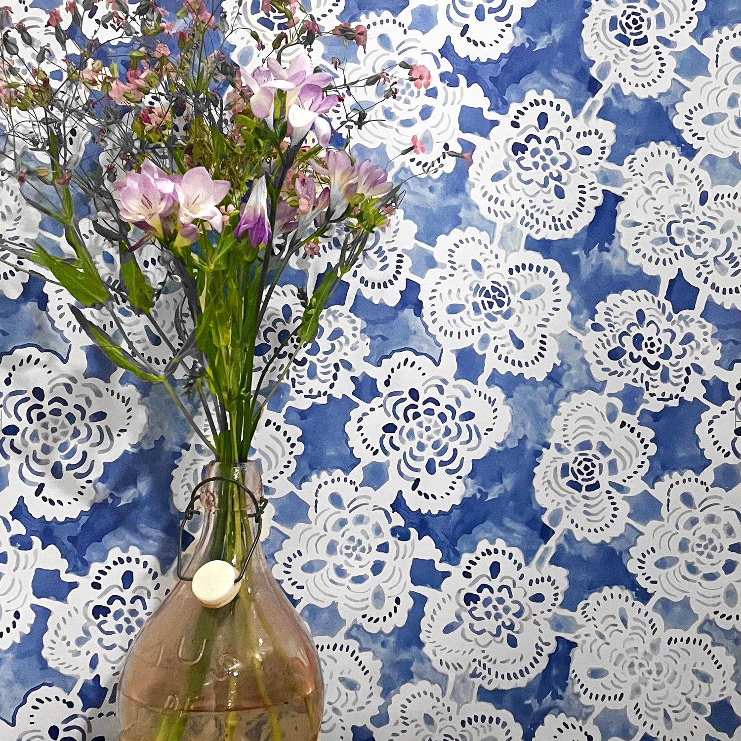 Vase with flowers against a blue wall with white lace patterns
