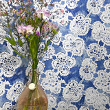 Vase with flowers against a blue wall with white lace patterns