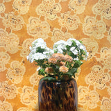 Vase with flowers against a decorative lace-patterned wall.