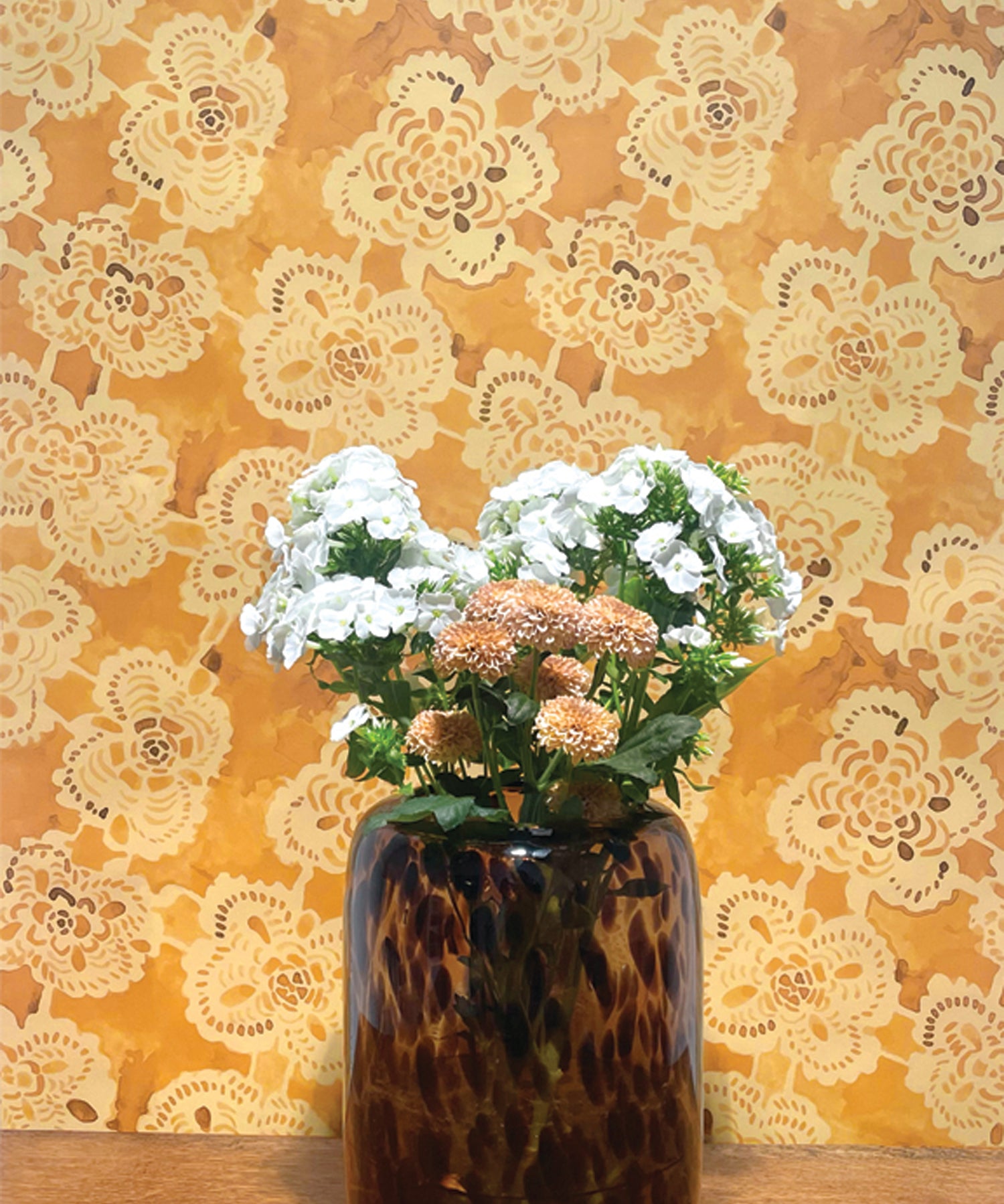 Vase with flowers against a decorative lace-patterned wall.