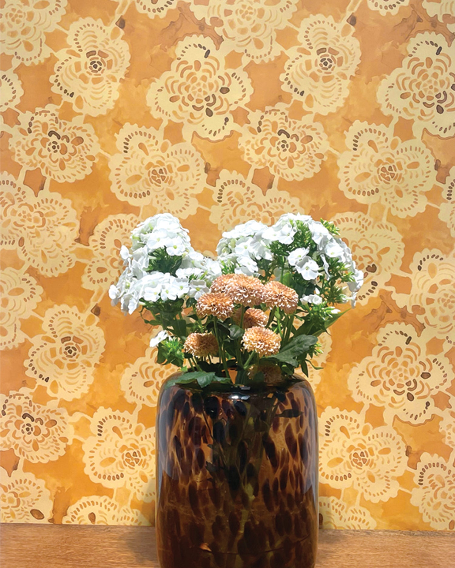 Vase with flowers against a decorative lace-patterned wall.