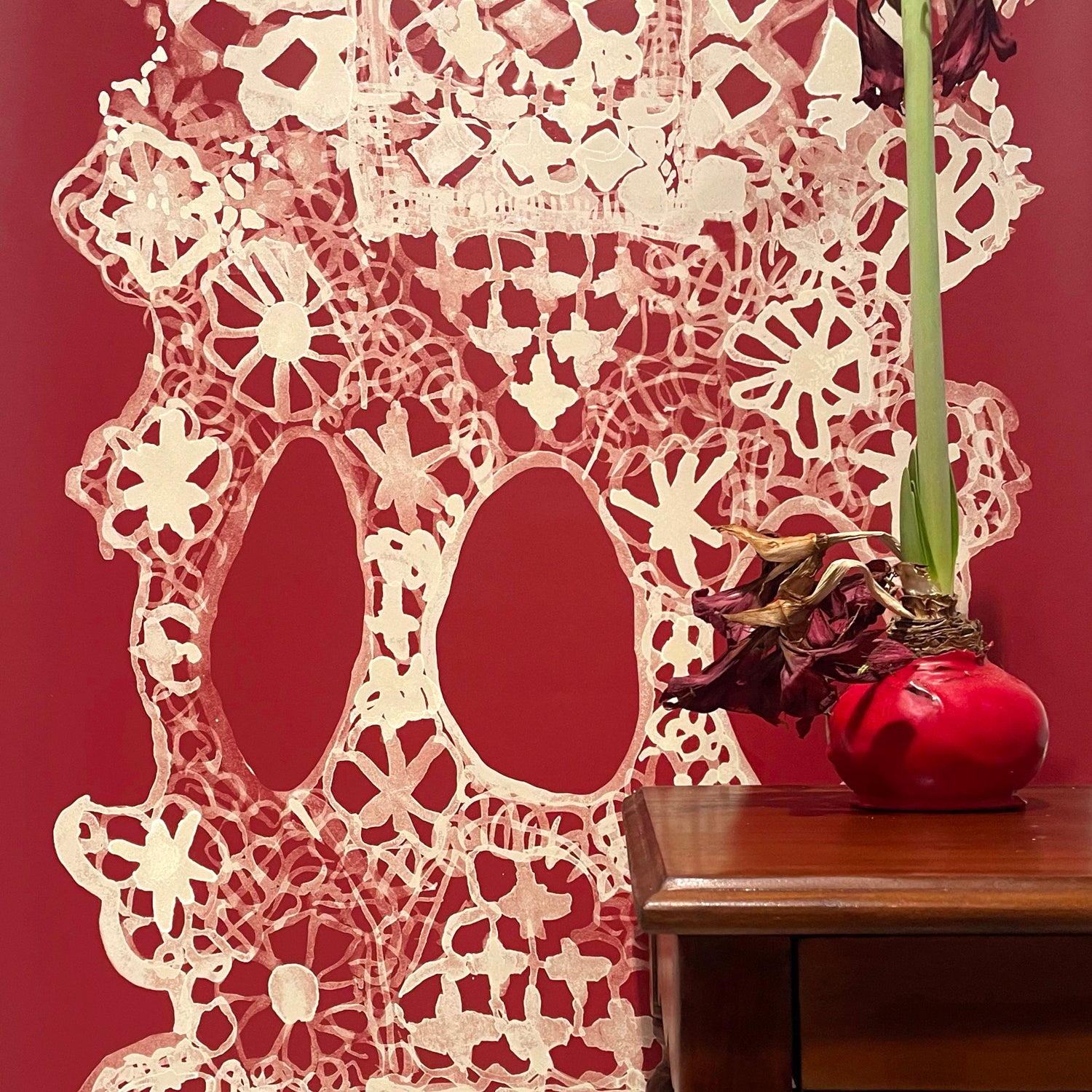 Decorative lace wallpaper in red with a vase on a wooden surface.