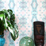 A plant and some knick knacks stand in front of a wall papered in a painterly gometric stripe in gray, blue, green and pink.