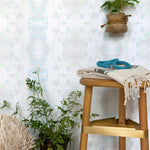 A stool and several plants stand in front of a wall papered in a painterly gometric stripe in gray, blue, green and white.