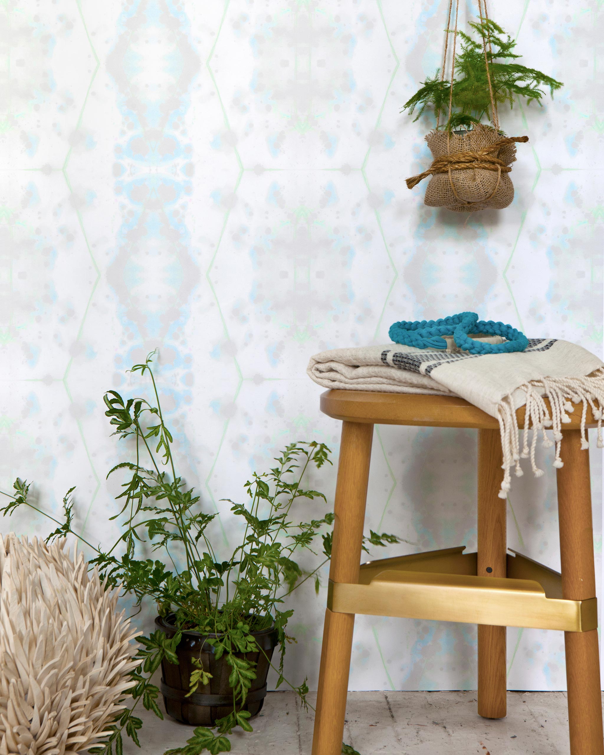 A stool and several plants stand in front of a wall papered in a painterly gometric stripe in gray, blue, green and white.