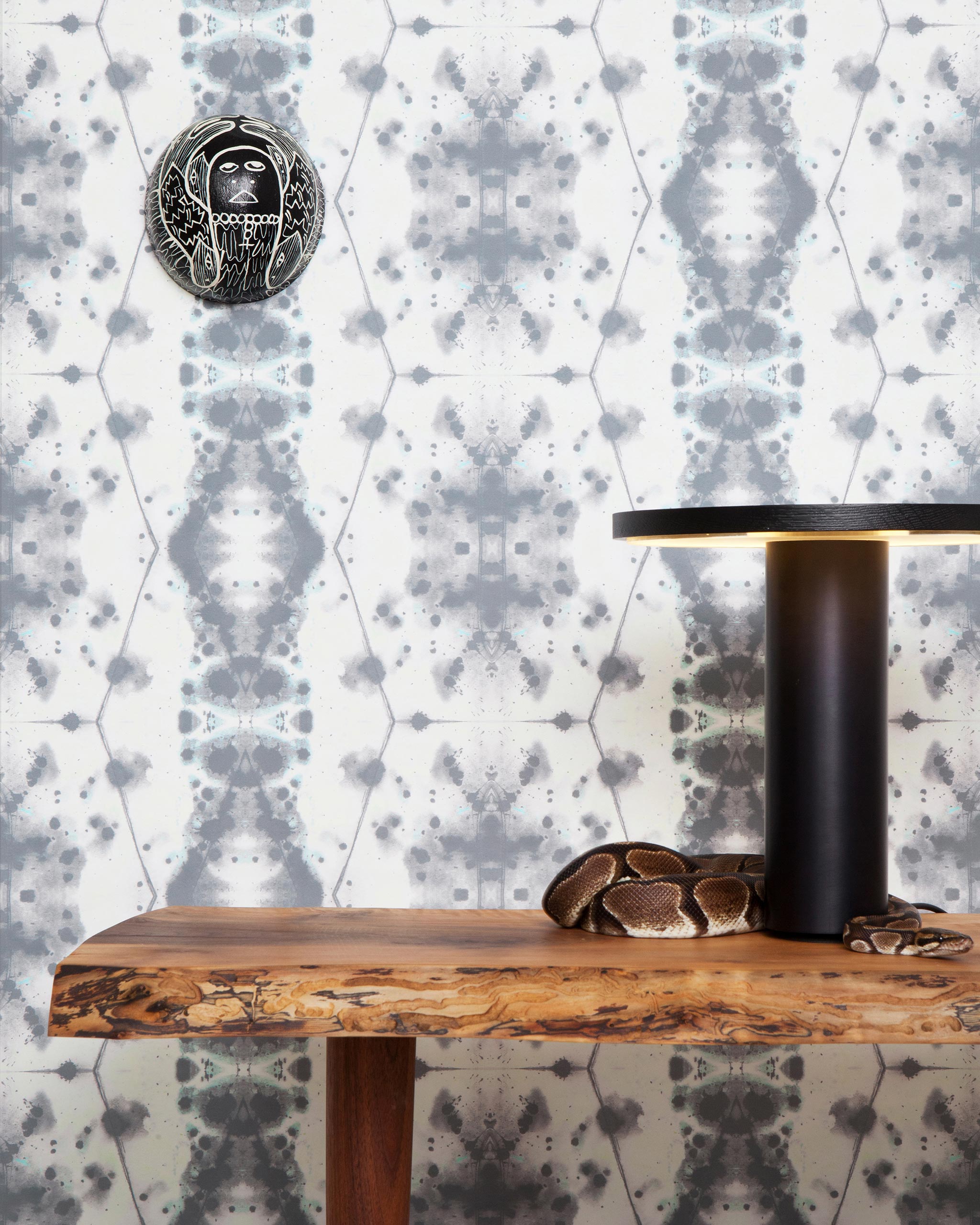 A wooden table with a snake on it stands in front of a wall papered in a painterly gometric stripe in gray, blue and cream.
