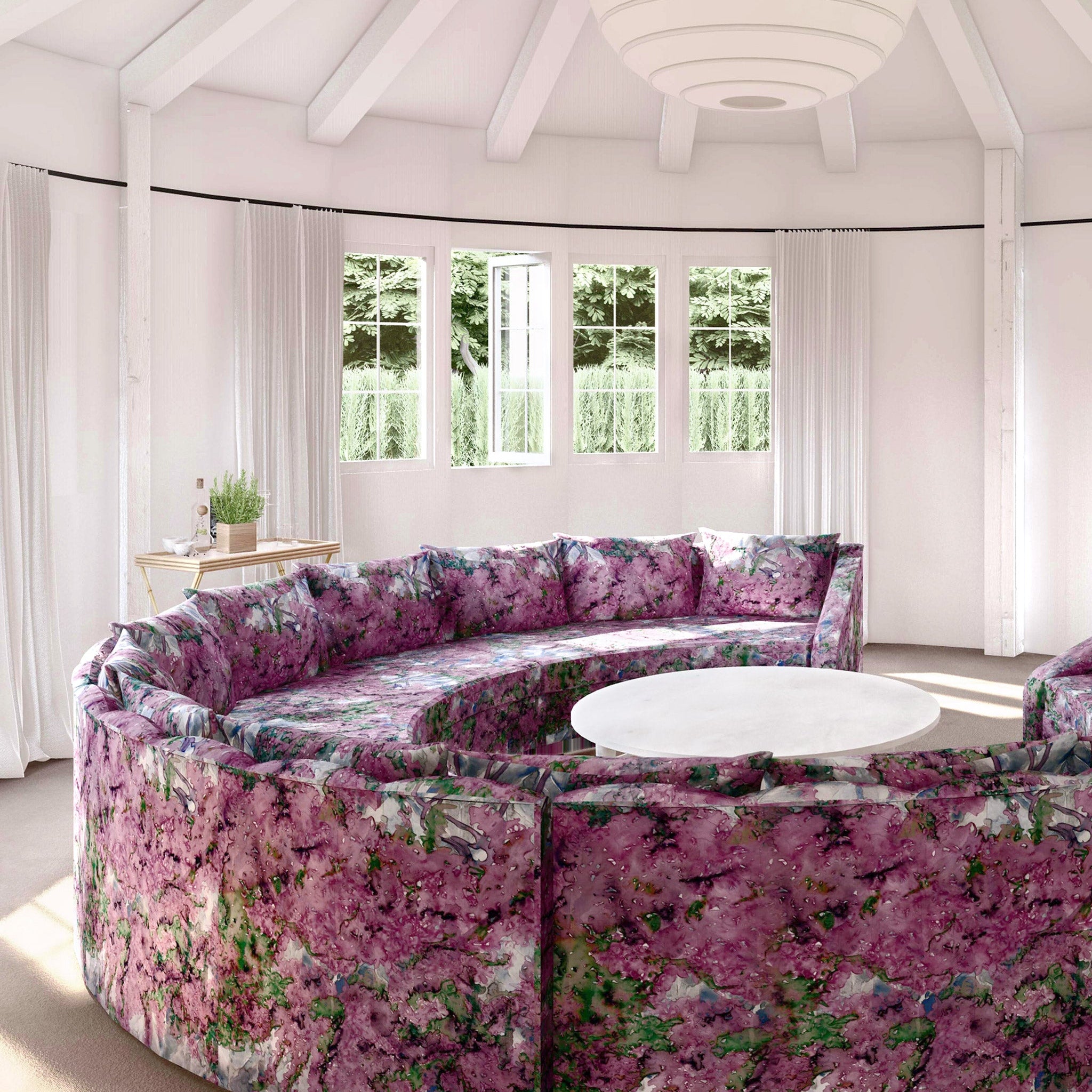 A large round sofa upholstered in a painterly botanical print in purple, green and brown stands in the middle of a sunny room.