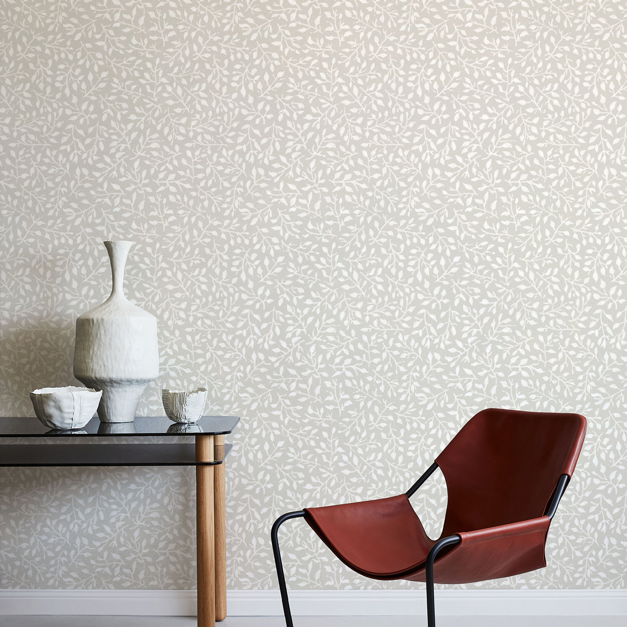 Modern brown chair and small table against a leaf patterned wall.