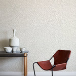 Modern brown chair and small table against a leaf patterned wall.