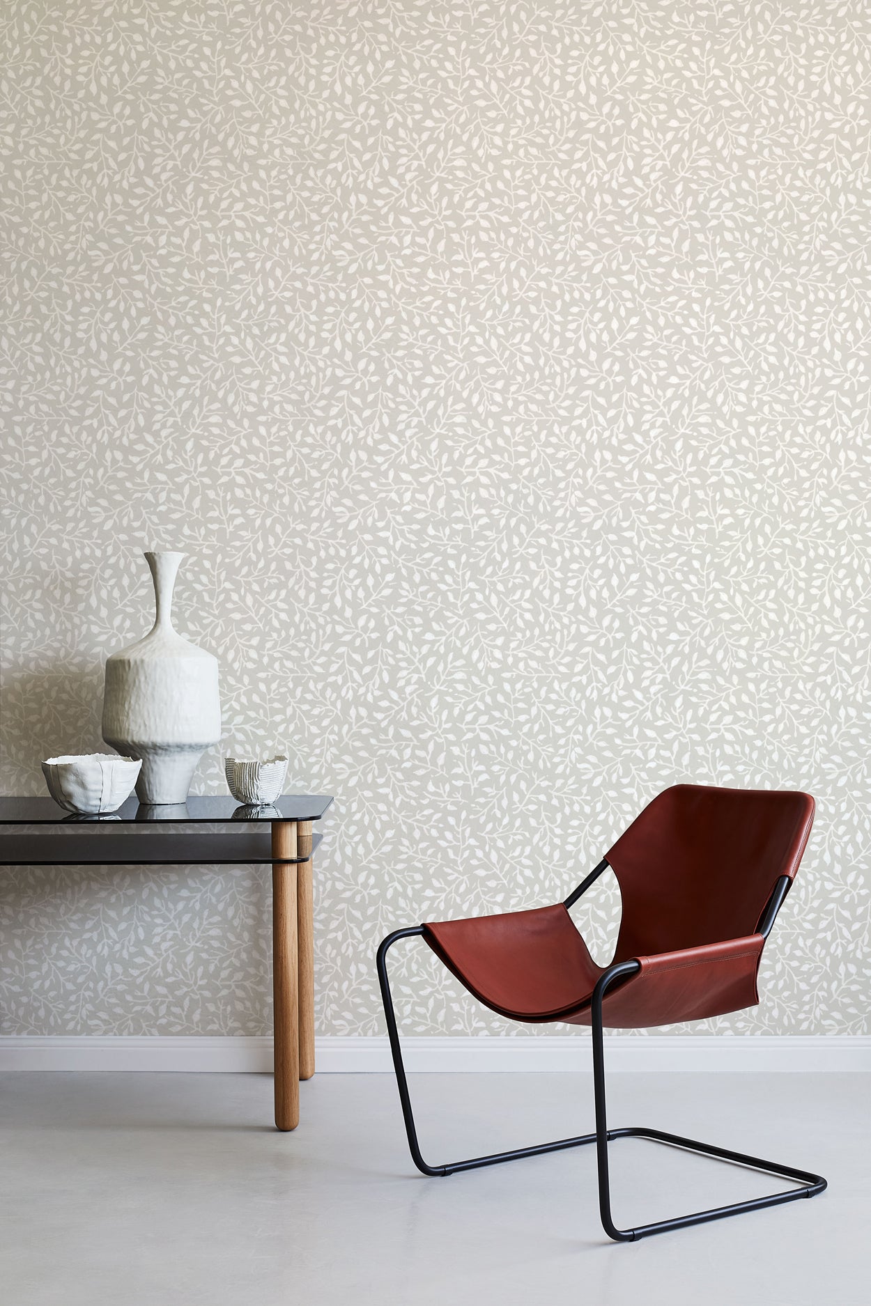 Modern brown chair and small table against a leaf patterned wall.