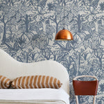 A modernist bed, hanging lamp and chair stand in front of a wall papered in a playful jungle print in blue and cream.