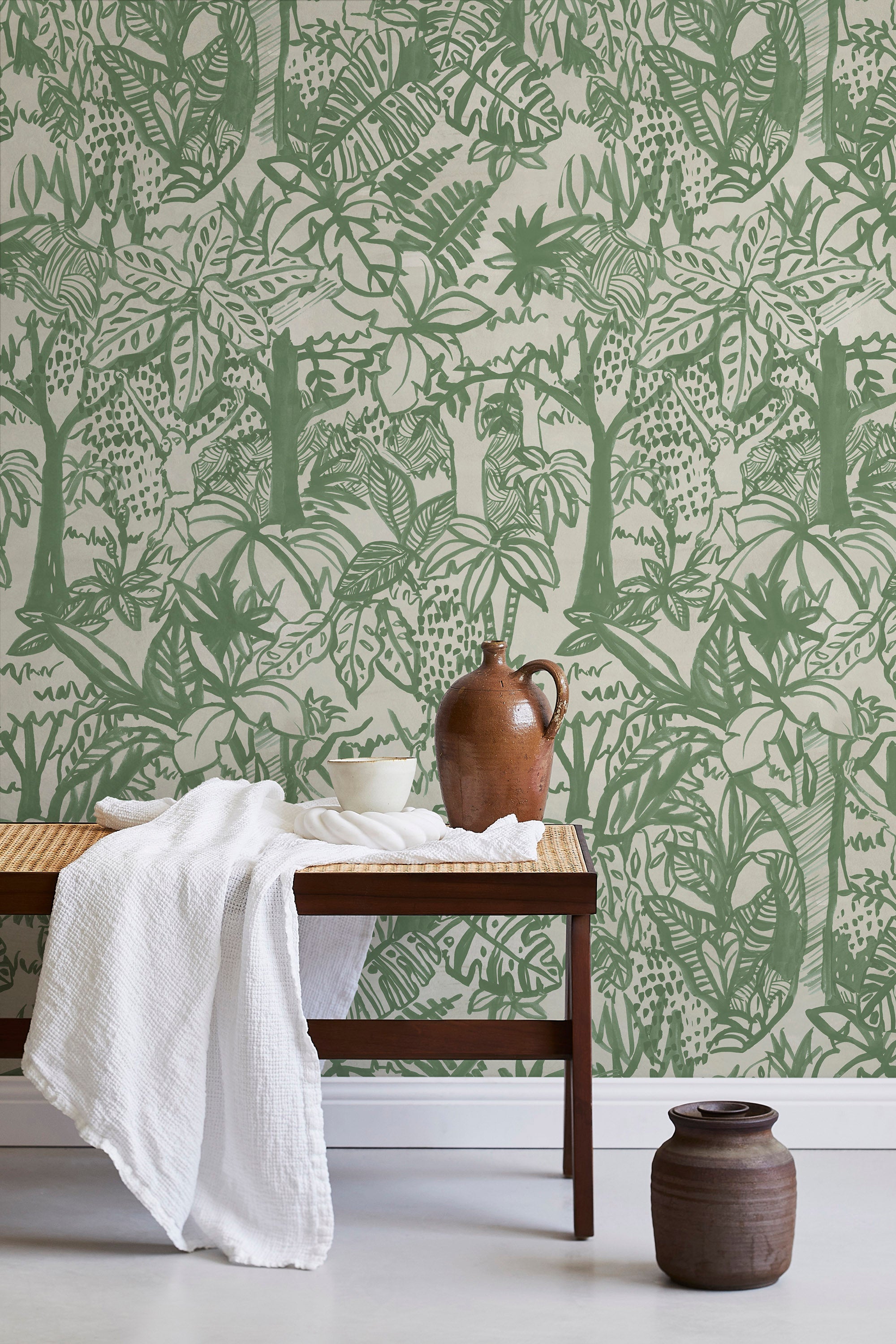 A bench with a towel and clay vases stands in front of a wall papered in a playful jungle print in green and cream.