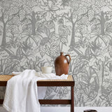 A bench with a towel and clay vases stands in front of a wall papered in a playful jungle print in gray and cream.