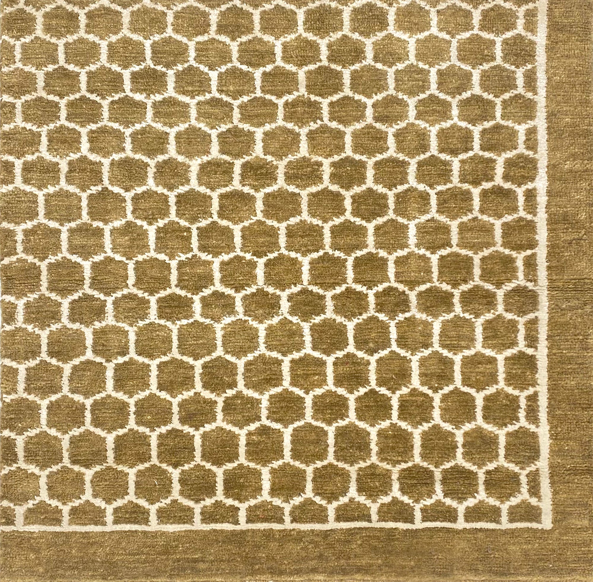 Handknotted rug sample in a small scale hex lattice in cream on an ochre field with a border at the right and bottom. 
