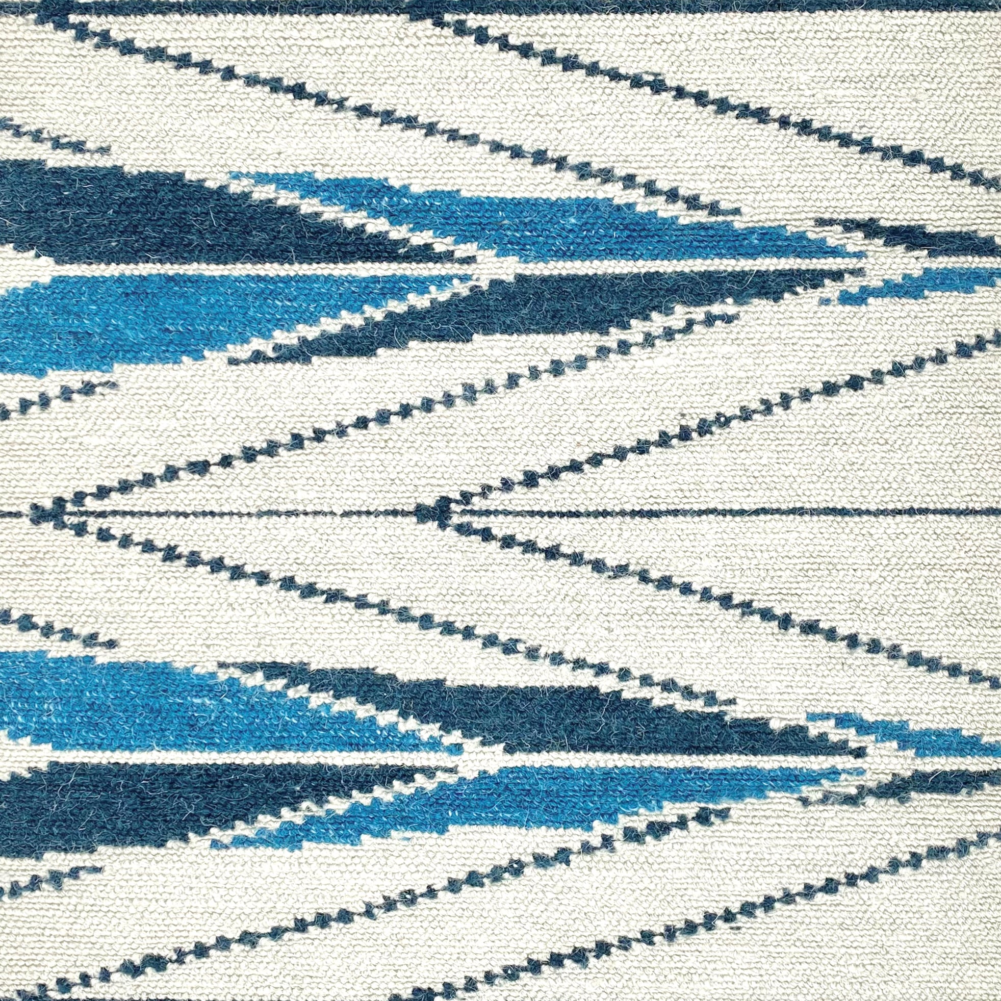 Handknotted rug sample in a modern herringbone design in shades of blue ona. white field. 
