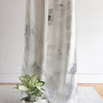 A potted plant sits on the floor in front of a curtain in a minimal splatter print in gray on a cream field.