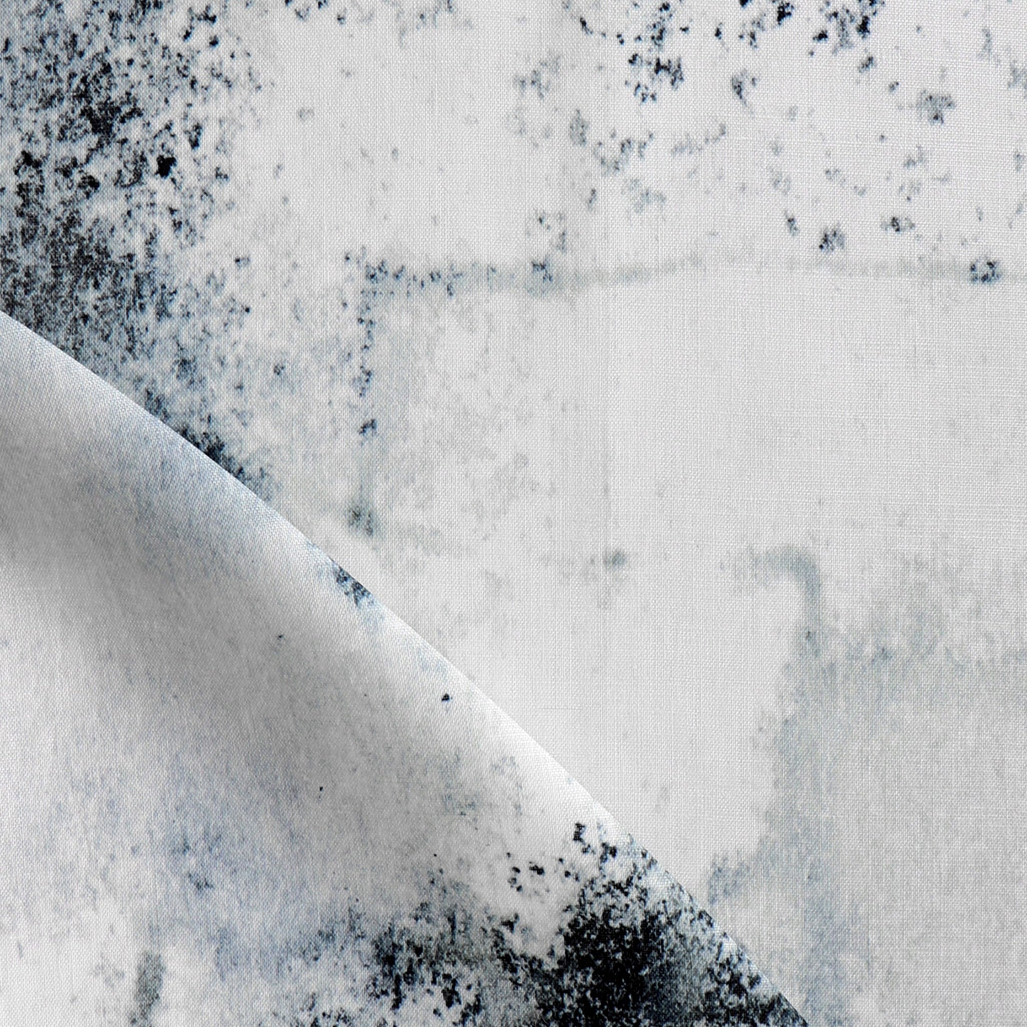 Detail of fabric in a minimal splatter print in shades of black and blue on a cream field.