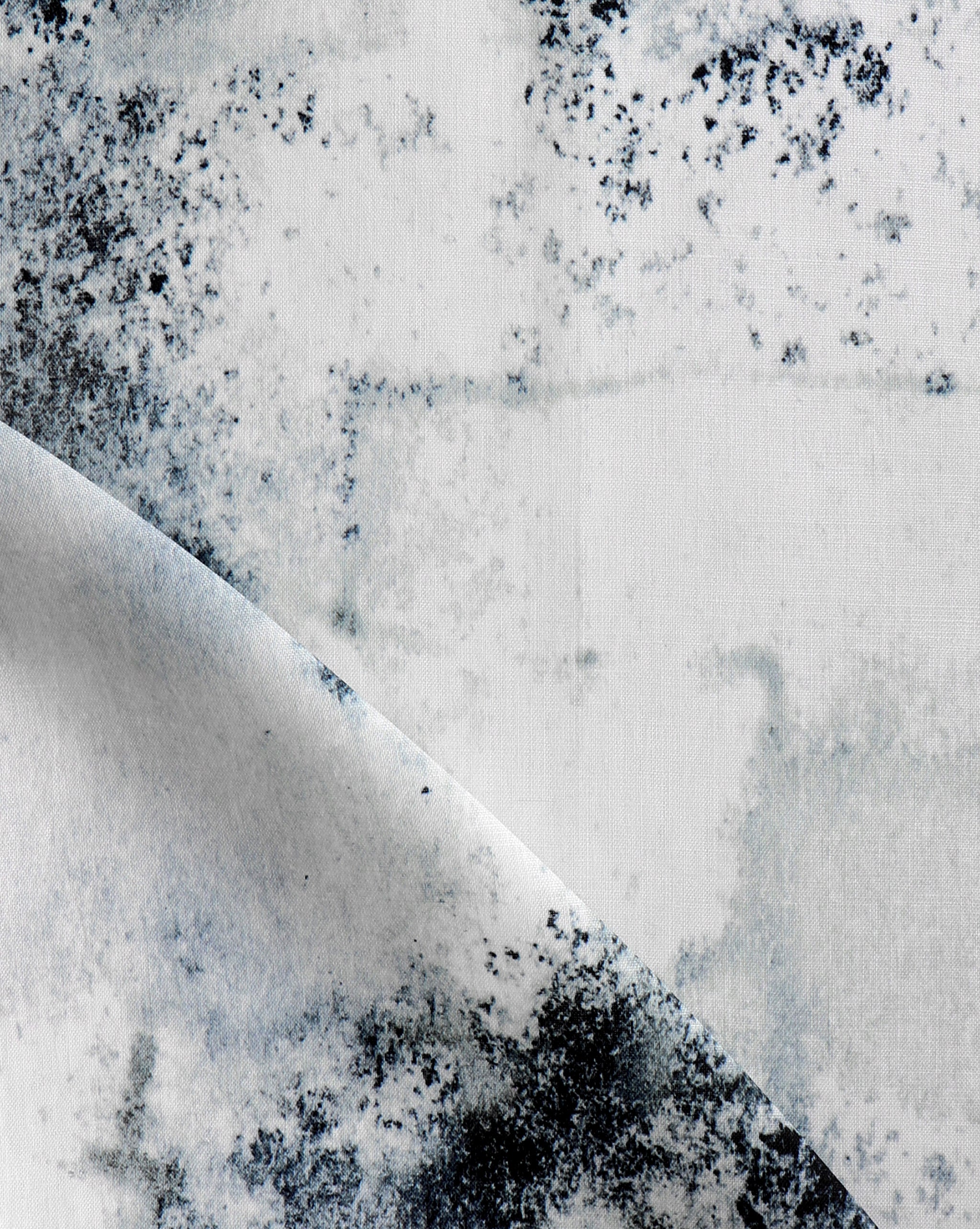 Detail of fabric in a minimal splatter print in shades of black and blue on a cream field.