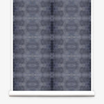 Partially unrolled wallpaper yardage in a repeating ink blot print in navy on a charcoal field.