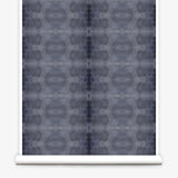 Partially unrolled wallpaper yardage in a repeating ink blot print in navy on a charcoal field.