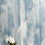 A vase of flowers stands in front of a wall papered in a linear geometric print in shades of blue and gray.