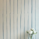 A vase of flowers stands in front of a wall covered in a playful irregular stripe print in blue on a cream field.