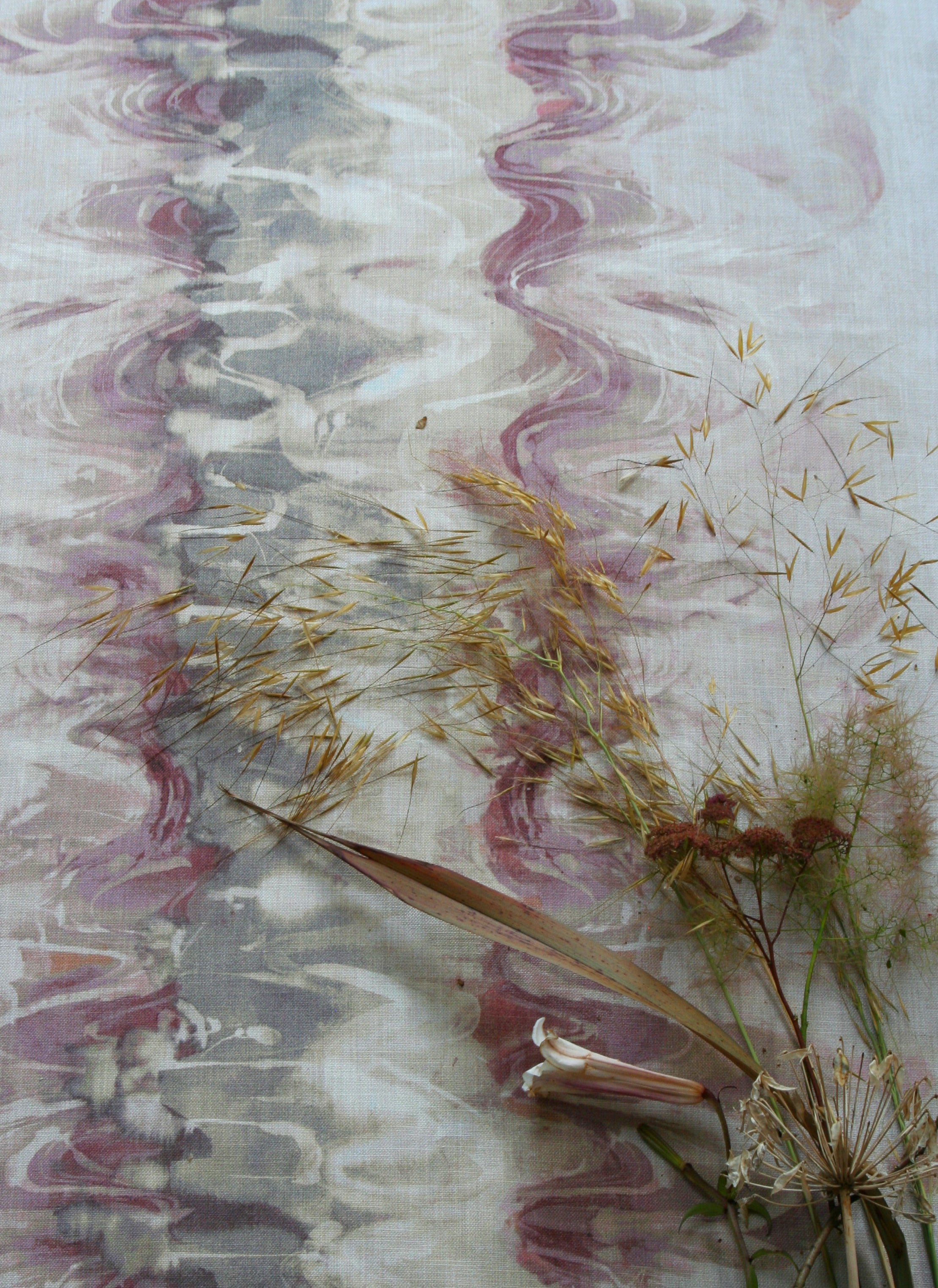 Flowers and branches lie on top of fabric yardage in an abstract paint blot pattern in shades of cream, gray and pink.