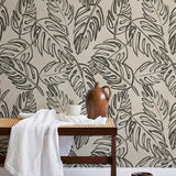 A bench with a towel and clay vases stands in front of a wall papered in a painterly leaf print in charcoal and cream.