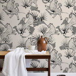 A bench with a towel and clay vases stands in front of a wall papered in a leopard and leaf print in gray and cream.