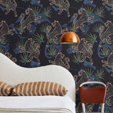 A modernist bed, hanging lamp and chair stand in front of a wall papered in a leopard and leaf print in pink and blue.